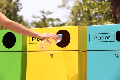 Woman throwing plastic bottle into sorting bin on city street, closeup. Recycling waste