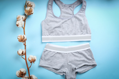 Photo of Sports women's underwear and cotton flowers on light blue background, flat lay
