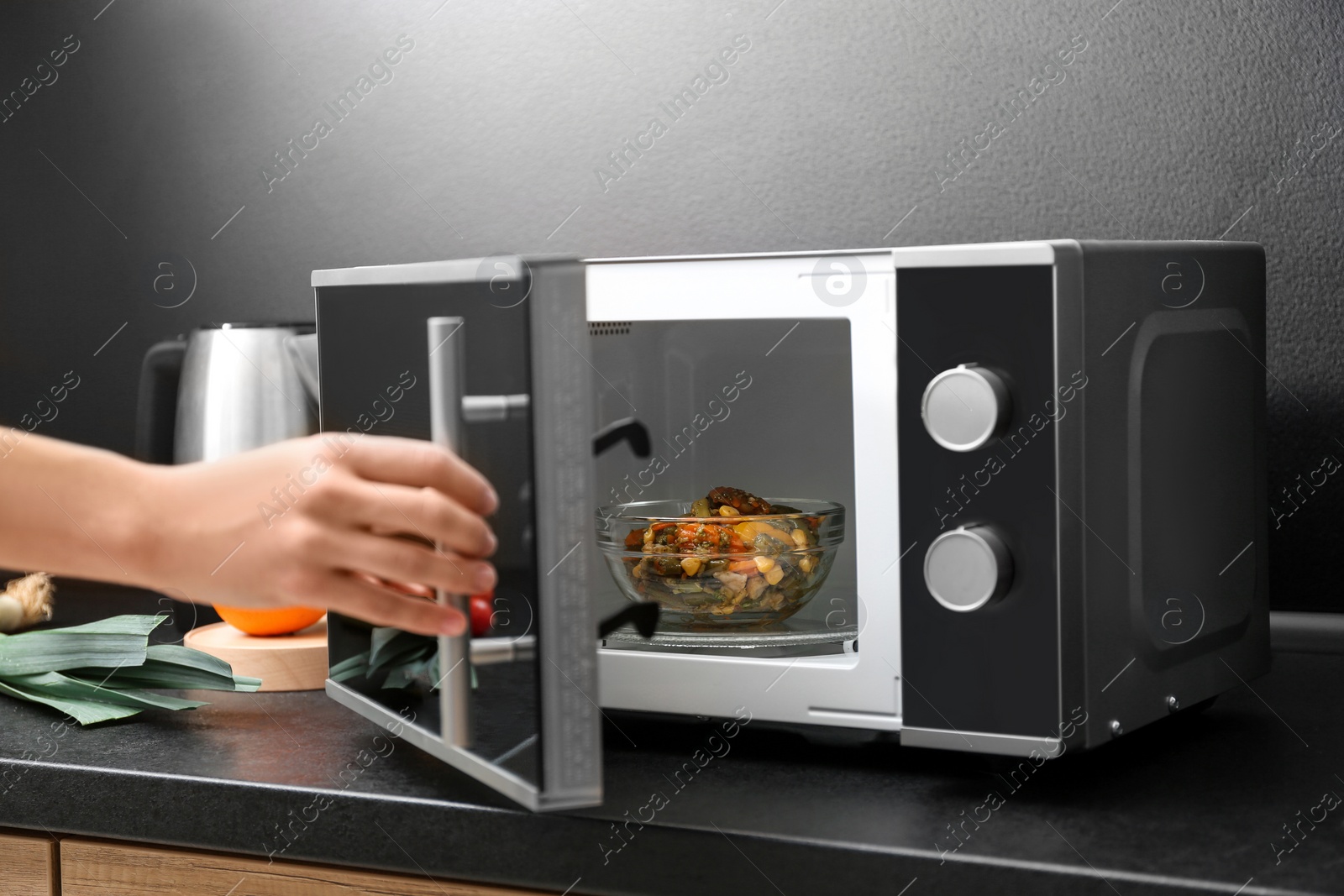 Photo of Young woman using microwave oven on table in kitchen