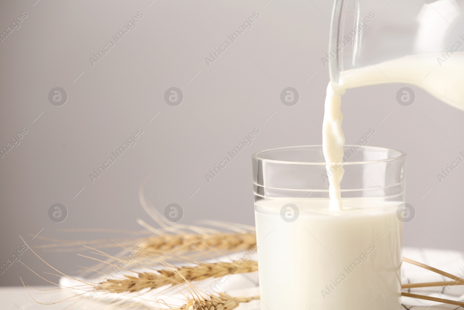 Photo of Pouring milk into glass on grey background. Space for text