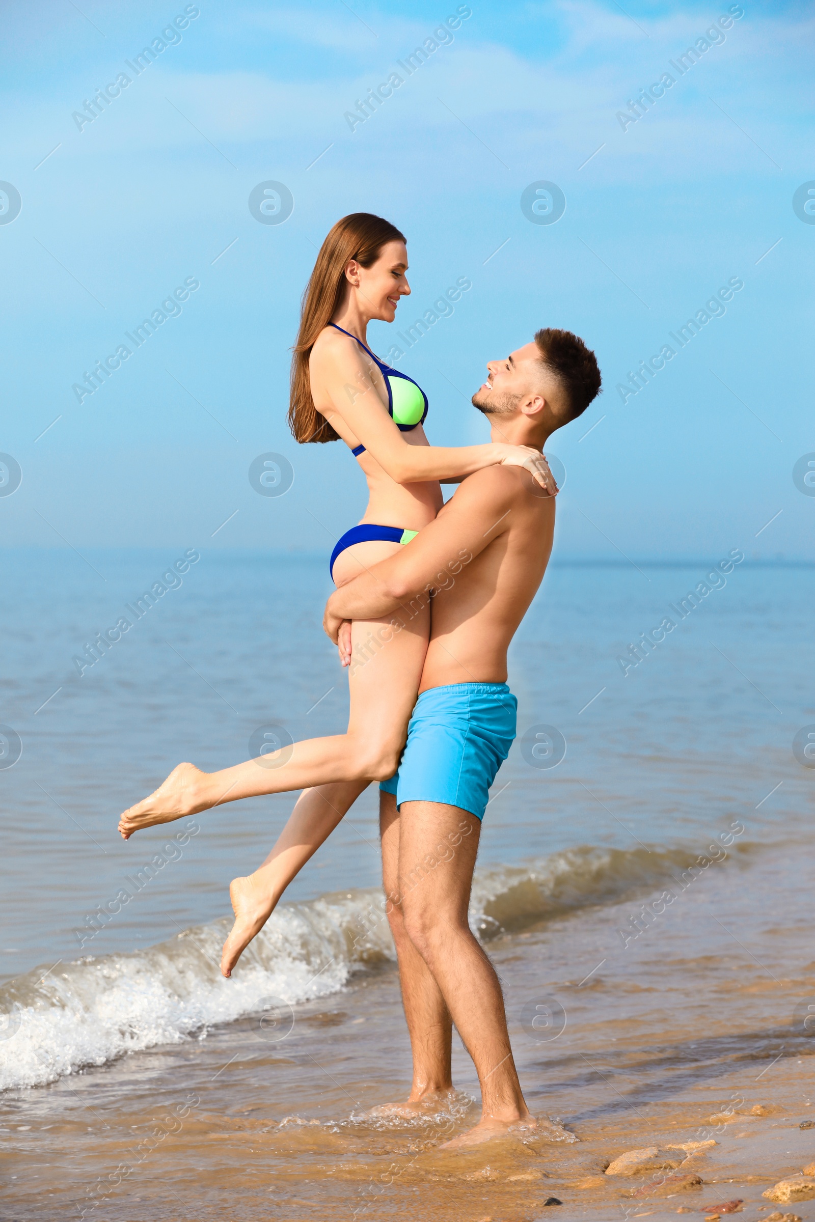 Photo of Young man holding his girlfriend in bikini on beach. Lovely couple