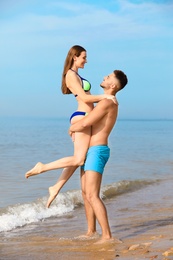 Photo of Young man holding his girlfriend in bikini on beach. Lovely couple