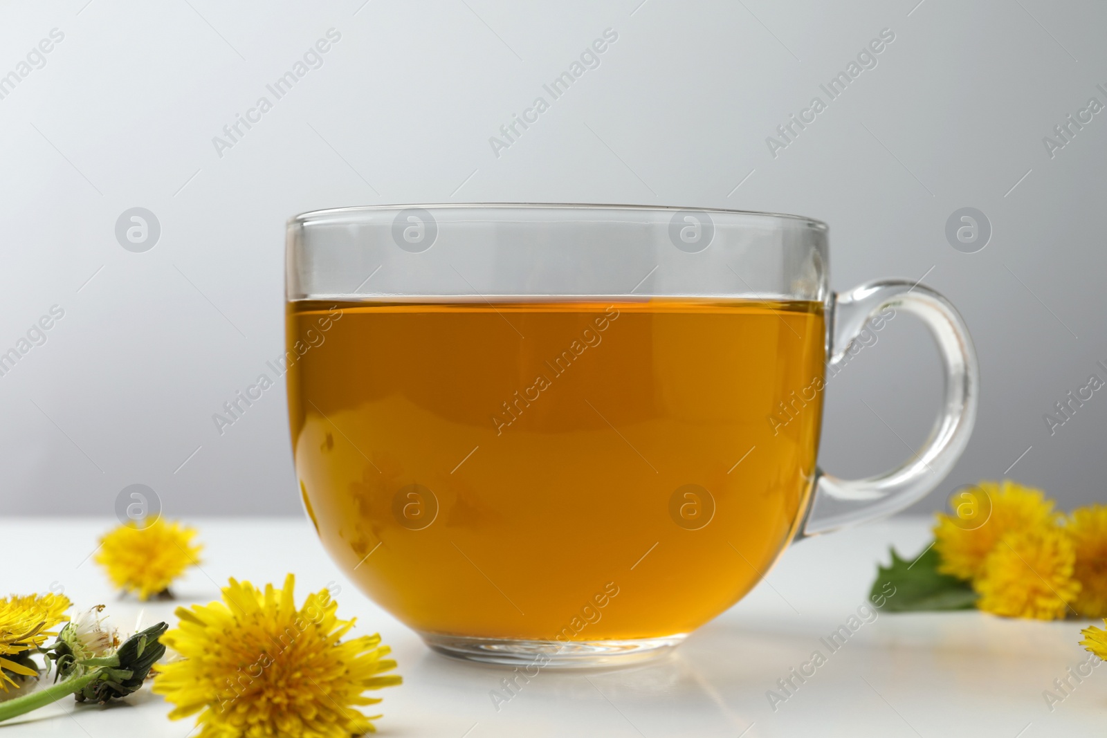 Photo of Delicious fresh tea and beautiful dandelion flowers on white table