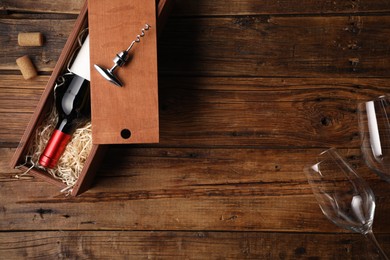 Photo of Box with wine bottle, glasses, corkscrew and corks on wooden table, flat lay