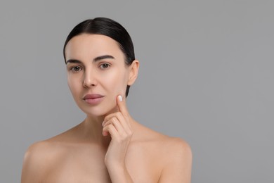 Woman with dry skin checking her face on gray background, space for text