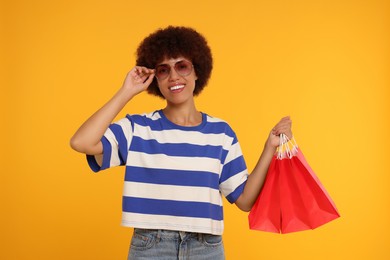 Photo of Happy young woman in stylish sunglasses with shopping bags on orange background