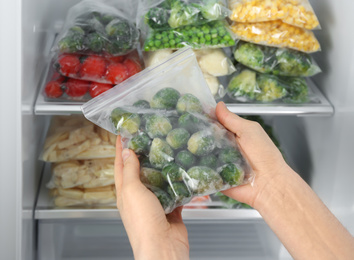 Photo of Woman holding plastic bag with frozen brussels sprouts near open refrigerator, closeup