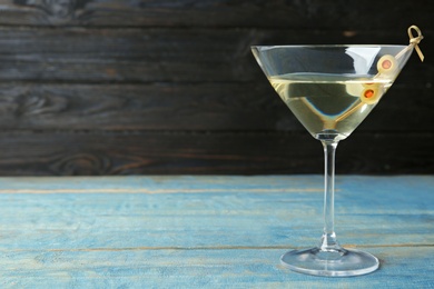 Photo of Glass of Classic Dry Martini with olives on light blue wooden table against dark background. Space for text
