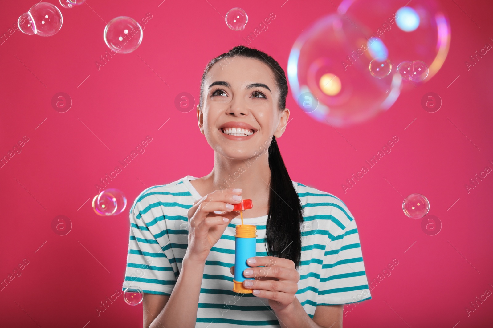 Photo of Young woman blowing soap bubbles on pink background