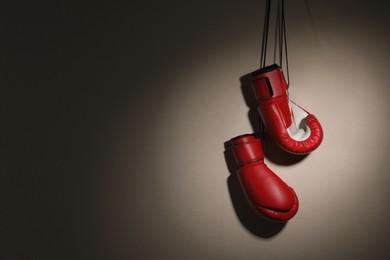 Photo of Pair of boxing gloves hanging on beige wall, space for text
