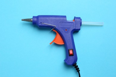 Glue gun with stick on light blue background, top view