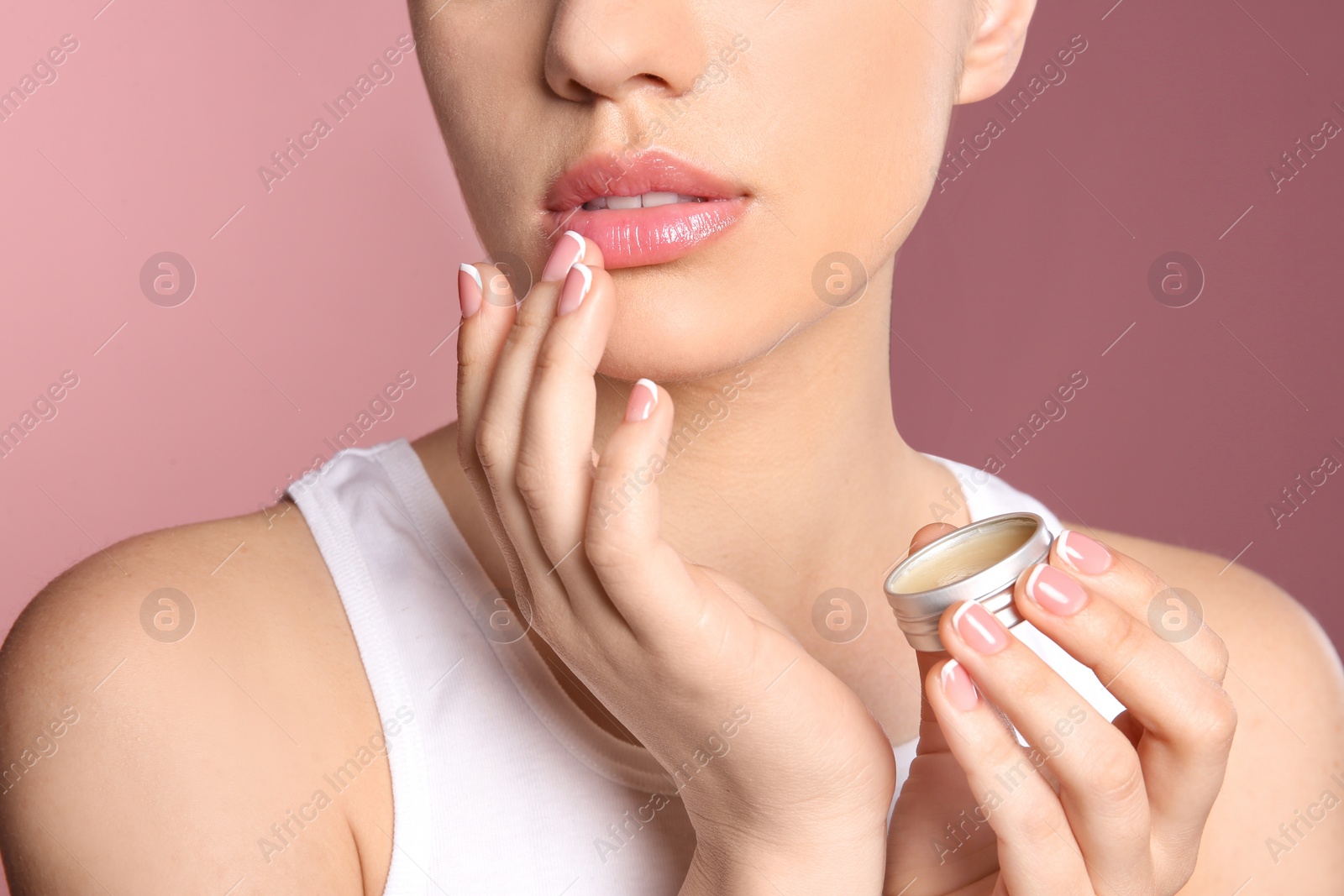 Photo of Young woman applying balm on her lips against color background, closeup