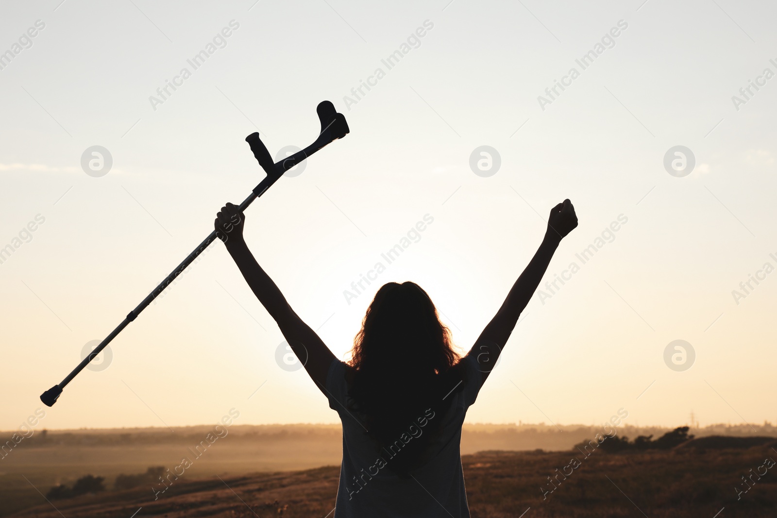 Photo of Woman holding elbow crutch outdoors at sunrise, back view. Healing miracle
