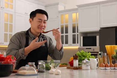 Photo of Cooking process. Man tasting salad in kitchen