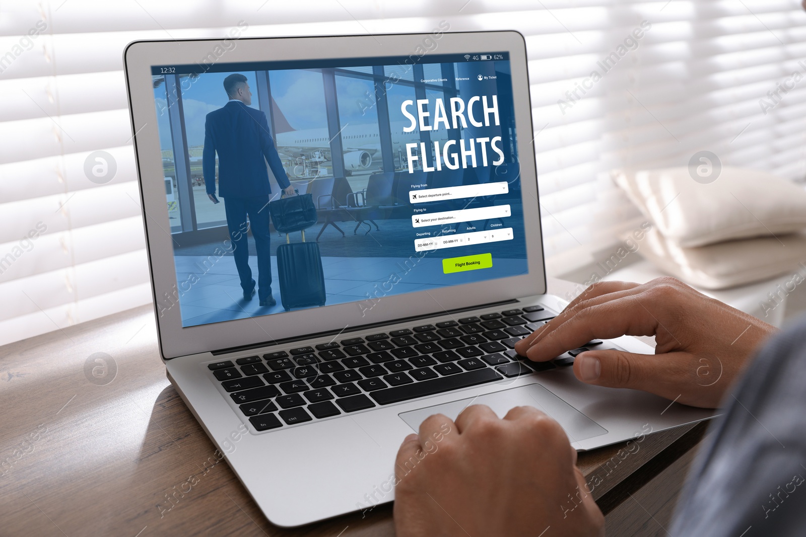 Image of Man using laptop to book flight at wooden table, closeup