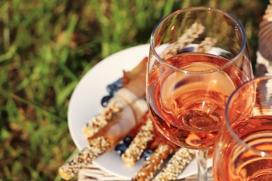 Photo of Glasses of delicious rose wine and food on wicker basket outdoors, closeup
