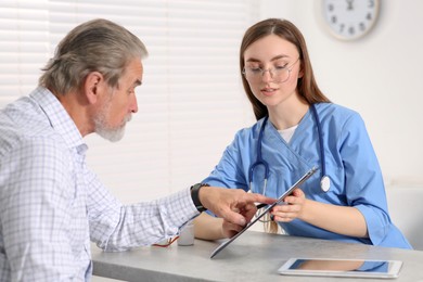 Photo of Doctor showing medical card to patient at table in clinic
