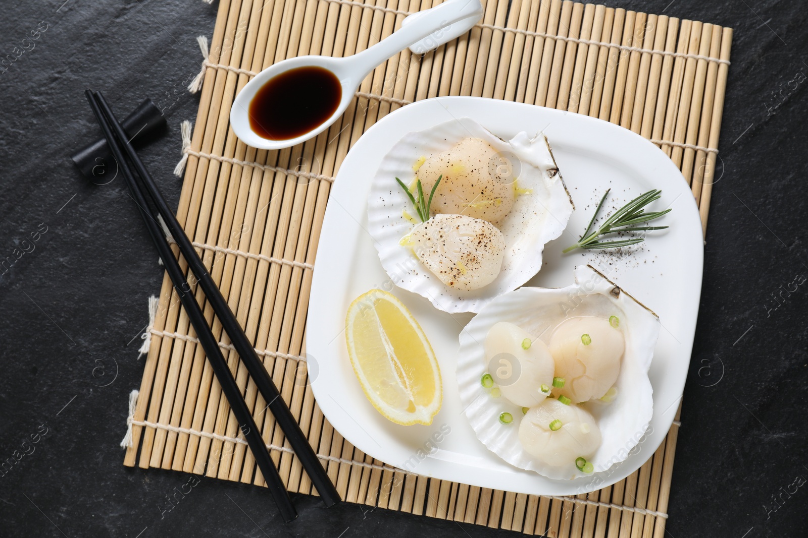 Photo of Raw scallops with green onion, rosemary, lemon and soy sauce on dark textured table, top view