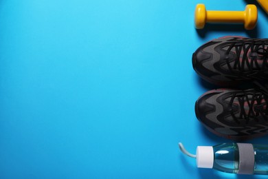 Sneakers, dumbbell and bottle of water on light blue background, flat lay with space for text. Morning exercise