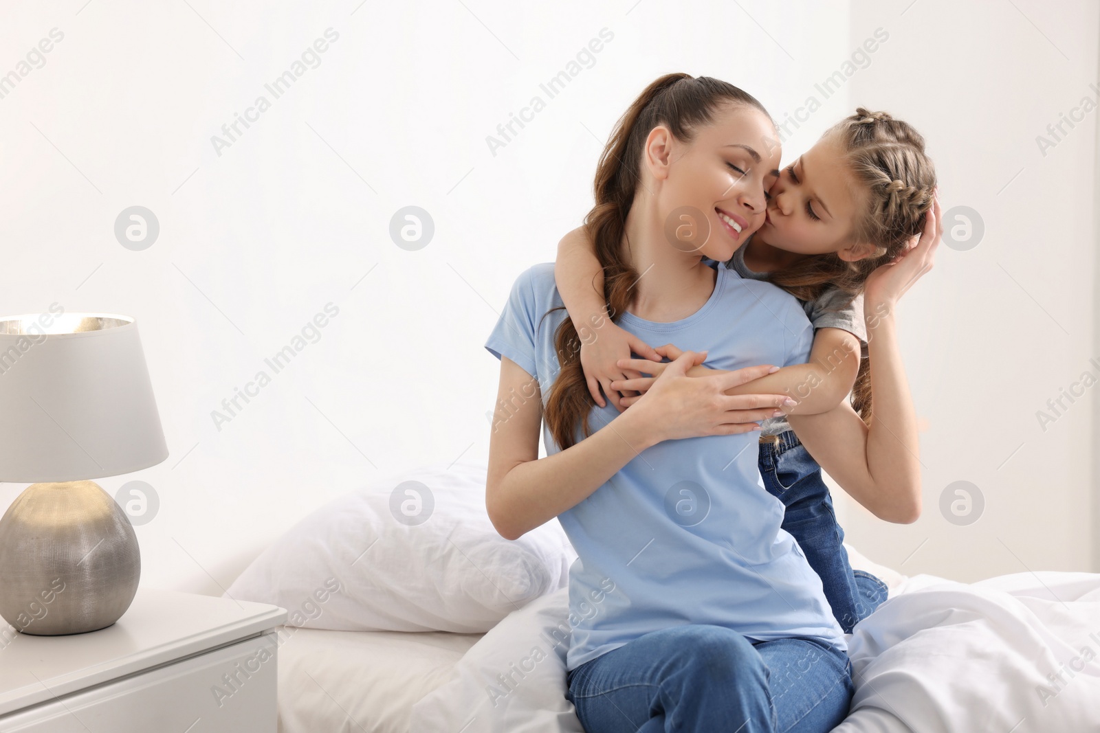 Photo of Cute daughter kissing her mom on bed at home