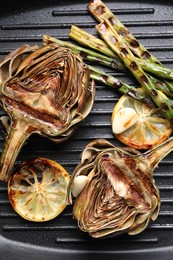 Photo of Tasty grilled artichokes, asparagus and slices of lemon in pan, top view