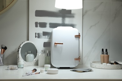 Photo of Cosmetics refrigerator and skin care products on white table indoors