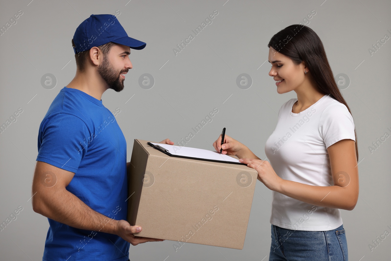 Photo of Smiling woman signing order receipt on grey background. Courier delivery