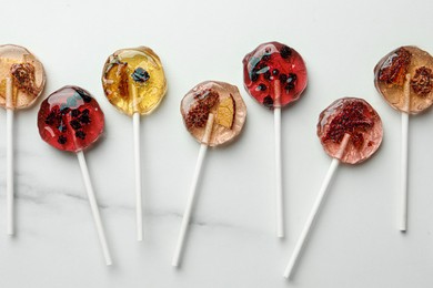 Photo of Sweet colorful lollipops with berries on white marble table, flat lay