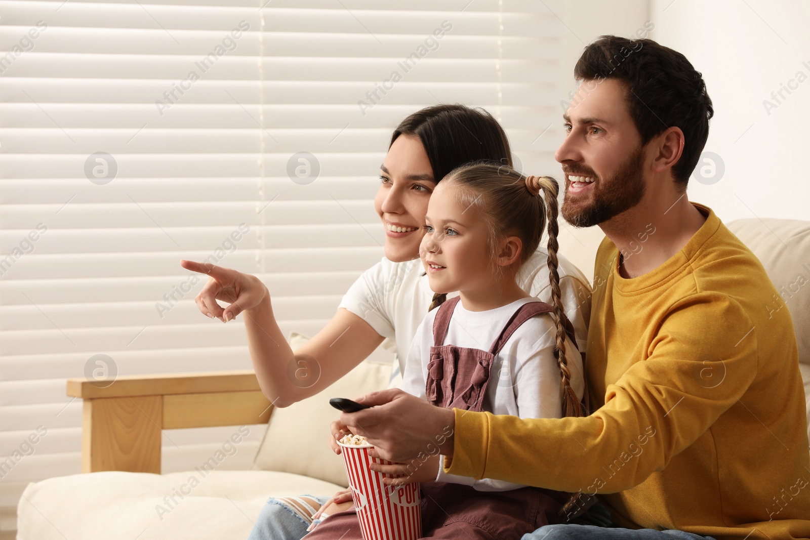 Photo of Happy family watching TV with popcorn on sofa indoors, space for text