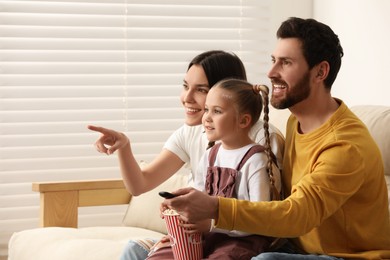 Happy family watching TV with popcorn on sofa indoors, space for text