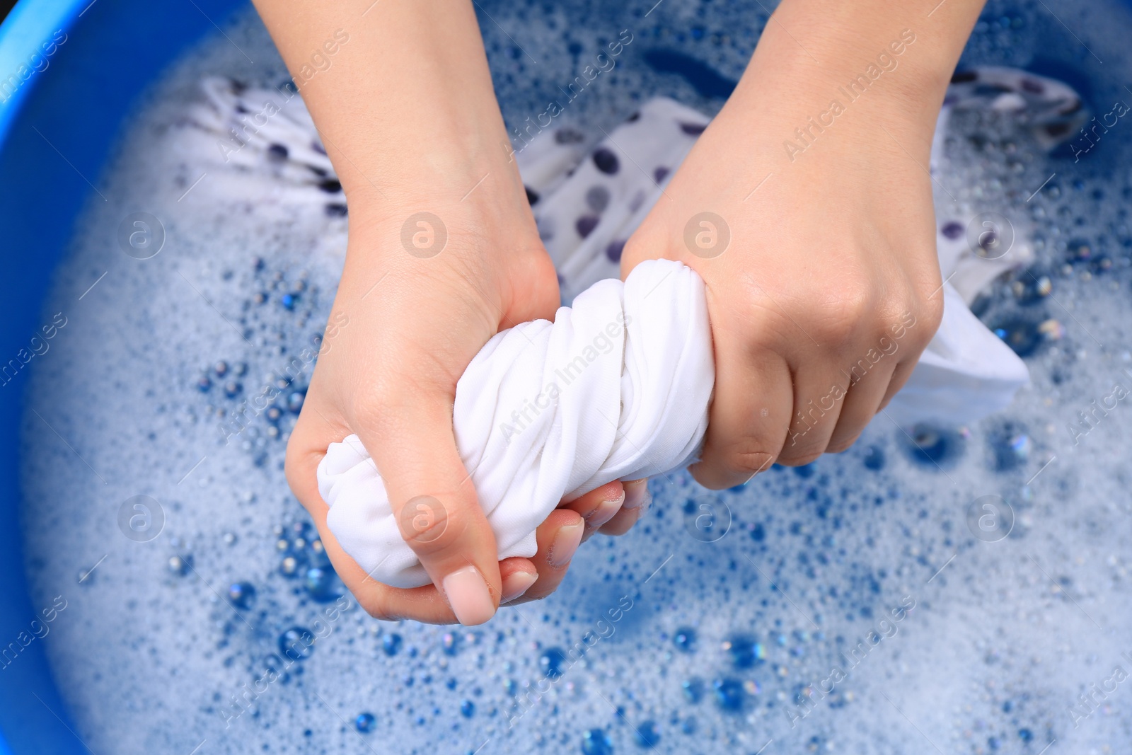 Photo of Woman wringing garment over basin, closeup. Hand washing laundry