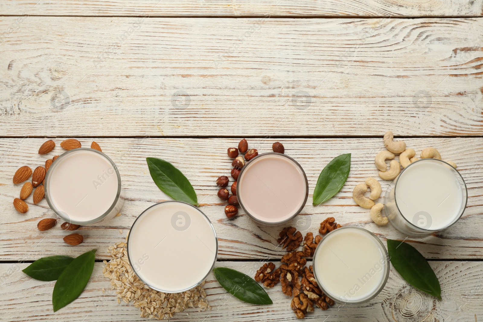 Photo of Different vegan milks and ingredients on white wooden table, flat lay. Space for text