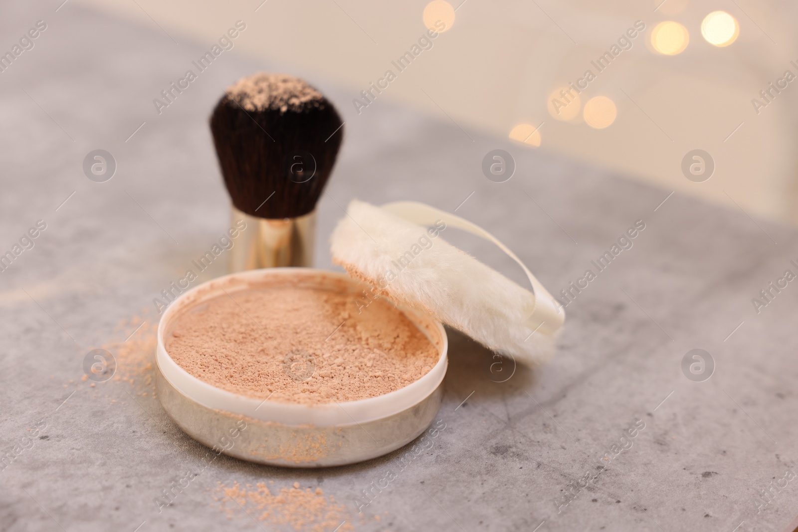Photo of Face powder and brush on grey textured table against blurred lights, closeup
