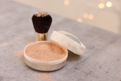 Photo of Face powder and brush on grey textured table against blurred lights, closeup