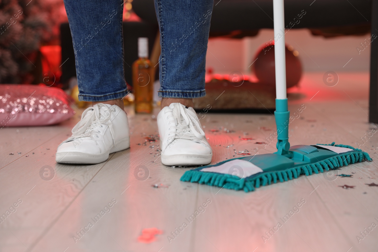 Photo of Man with mop cleaning messy room after New Year party, closeup of legs