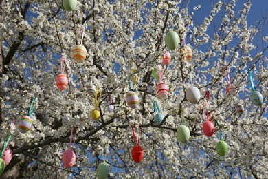 Photo of Beautifully painted Easter eggs hanging on blooming cherry tree outdoors