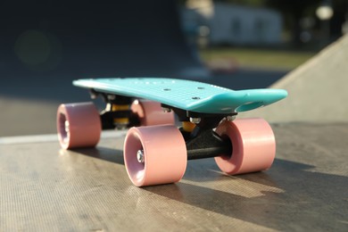Photo of Modern light blue skateboard with pink wheels on top of ramp outdoors, closeup