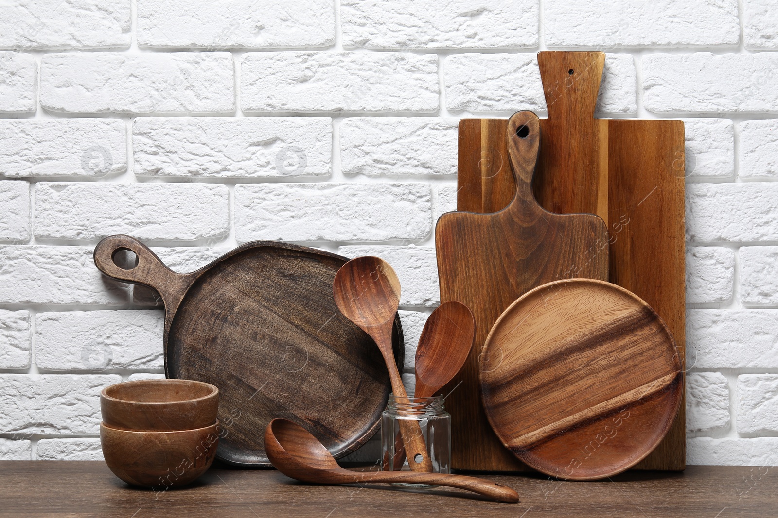 Photo of Different cutting boards, kitchen utensils and dishware on wooden table near white brick wall