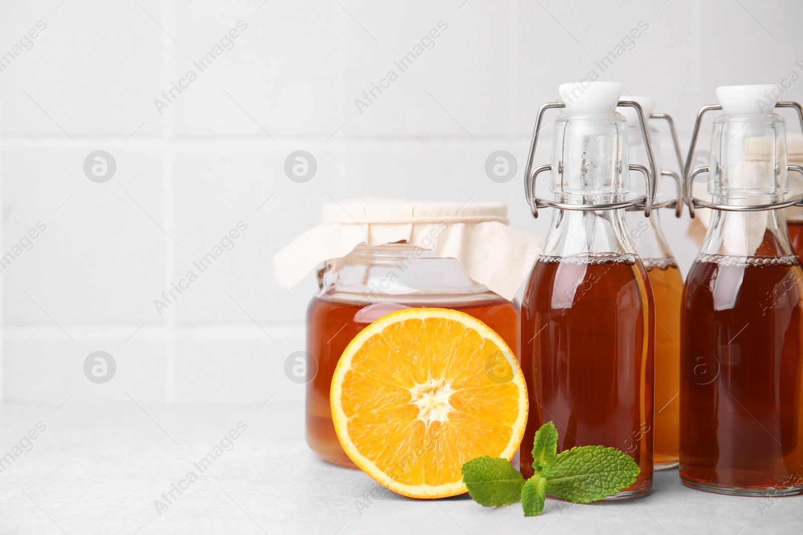 Photo of Tasty kombucha, orange and mint on white table, space for text