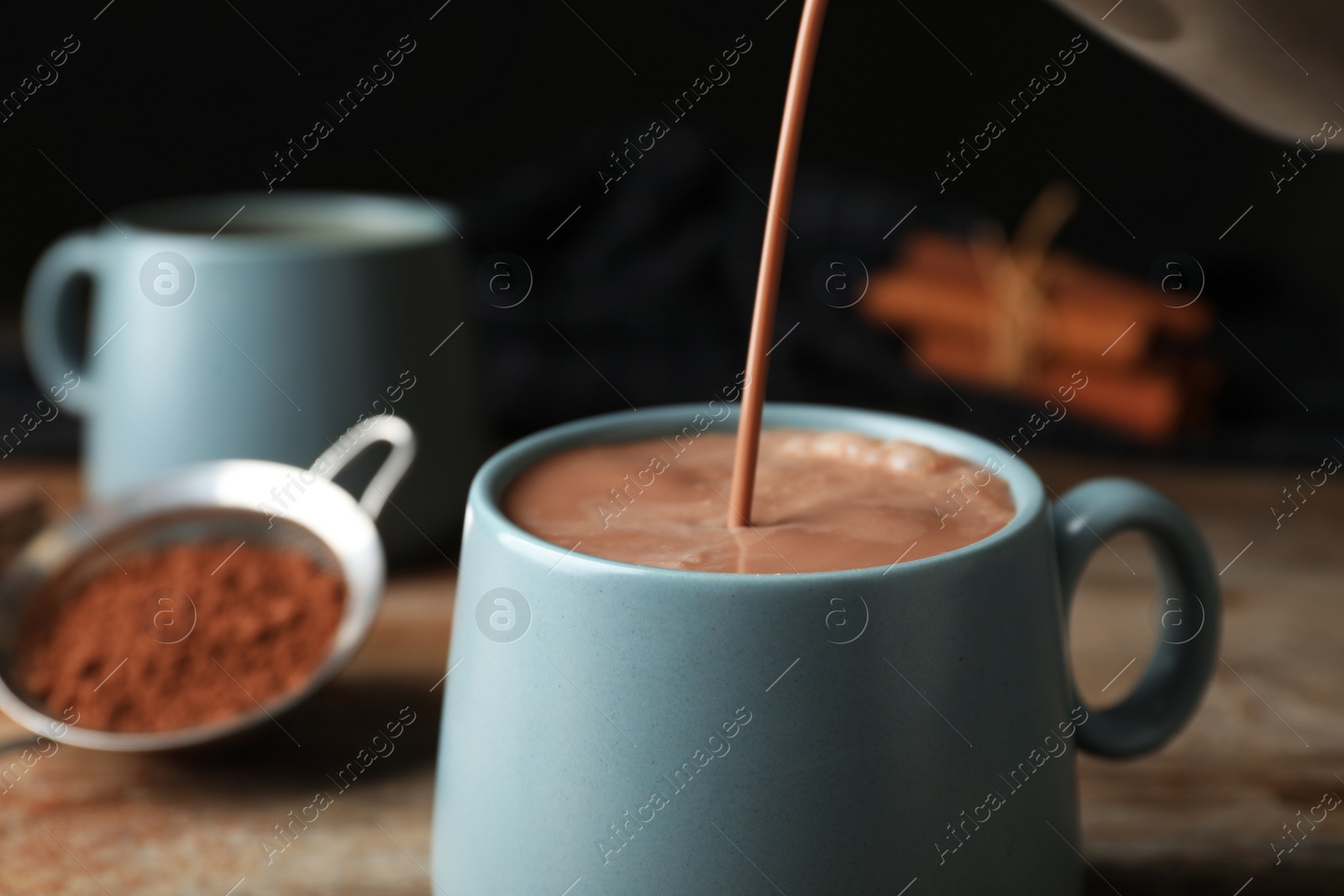 Photo of Pouring hot cocoa drink into cup on wooden table