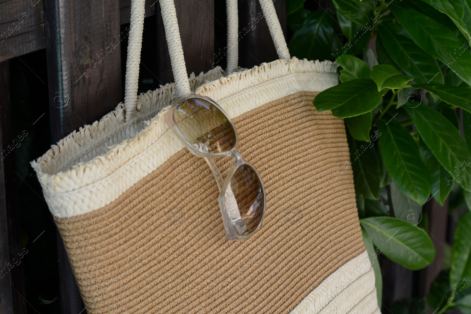 Photo of Stylish bag with sunglasses hanging on wooden fence outdoors, closeup. Beach accessories