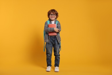 Photo of Happy schoolboy with backpack and books on orange background