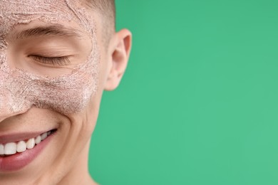Photo of Handsome man with facial mask on his face against green background, closeup. Space for text