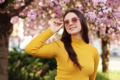 Photo of Beautiful woman in sunglasses near blossoming tree on spring day