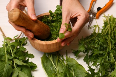 Photo of Woman grinding fresh green herbs in mortar at white wooden table, closeup