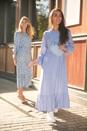 Beautiful young women in stylish blue dresses on city street