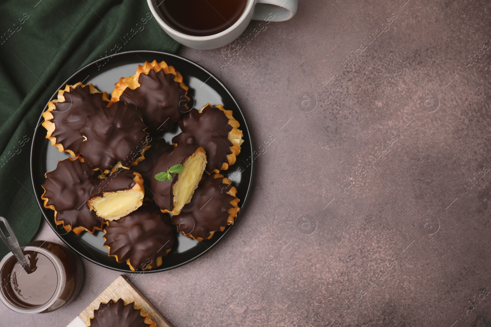 Photo of Delicious profiteroles with chocolate spread, cream and aromatic tea on textured table, flat lay. Space for text