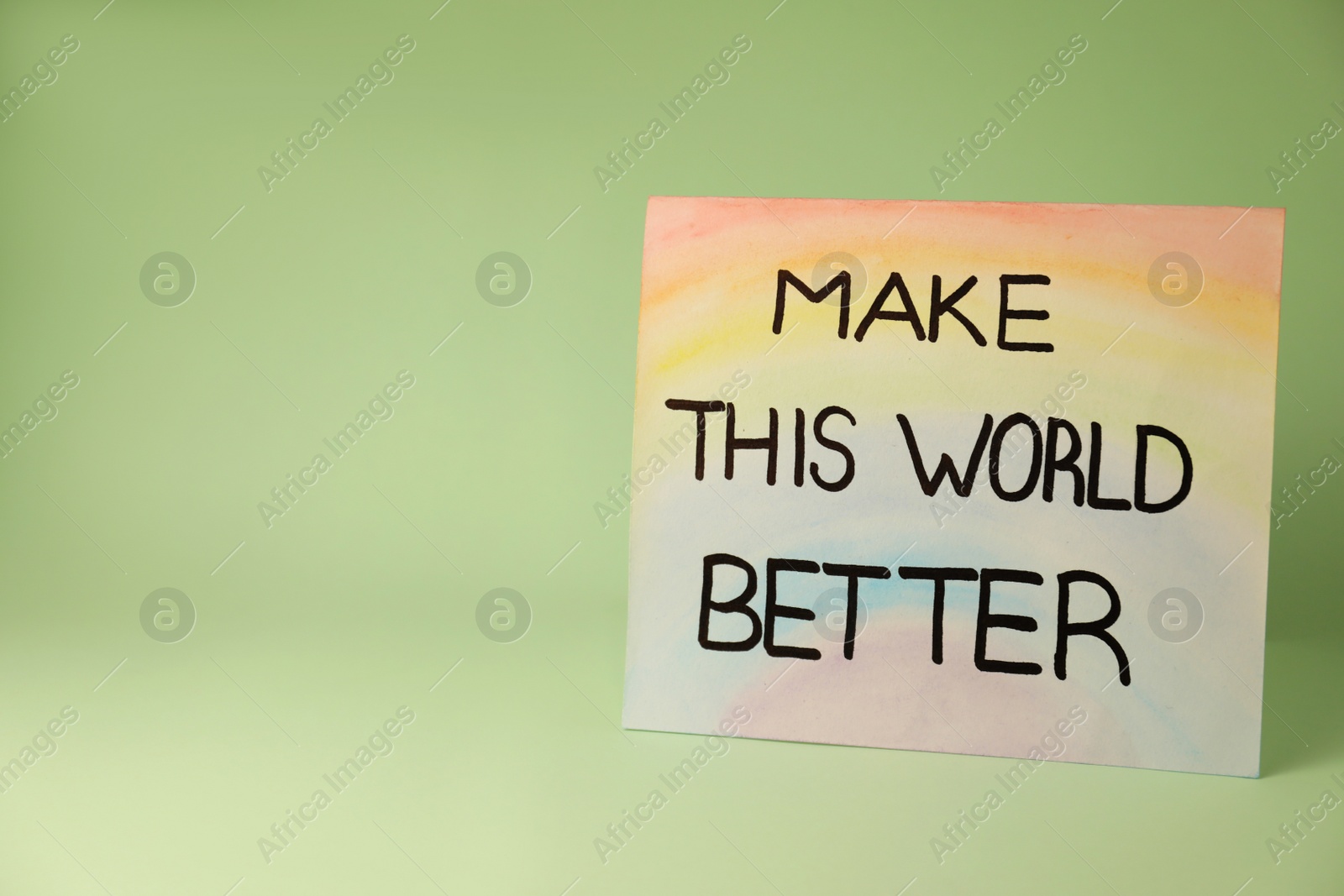 Photo of Card with phrase Make This World Better on pastel green background. Space for text