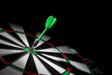 Photo of Green arrow hitting target on dart board against black background. Space for text