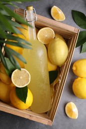 Photo of Tasty limoncello liqueur, lemons and green leaves on grey table, flat lay